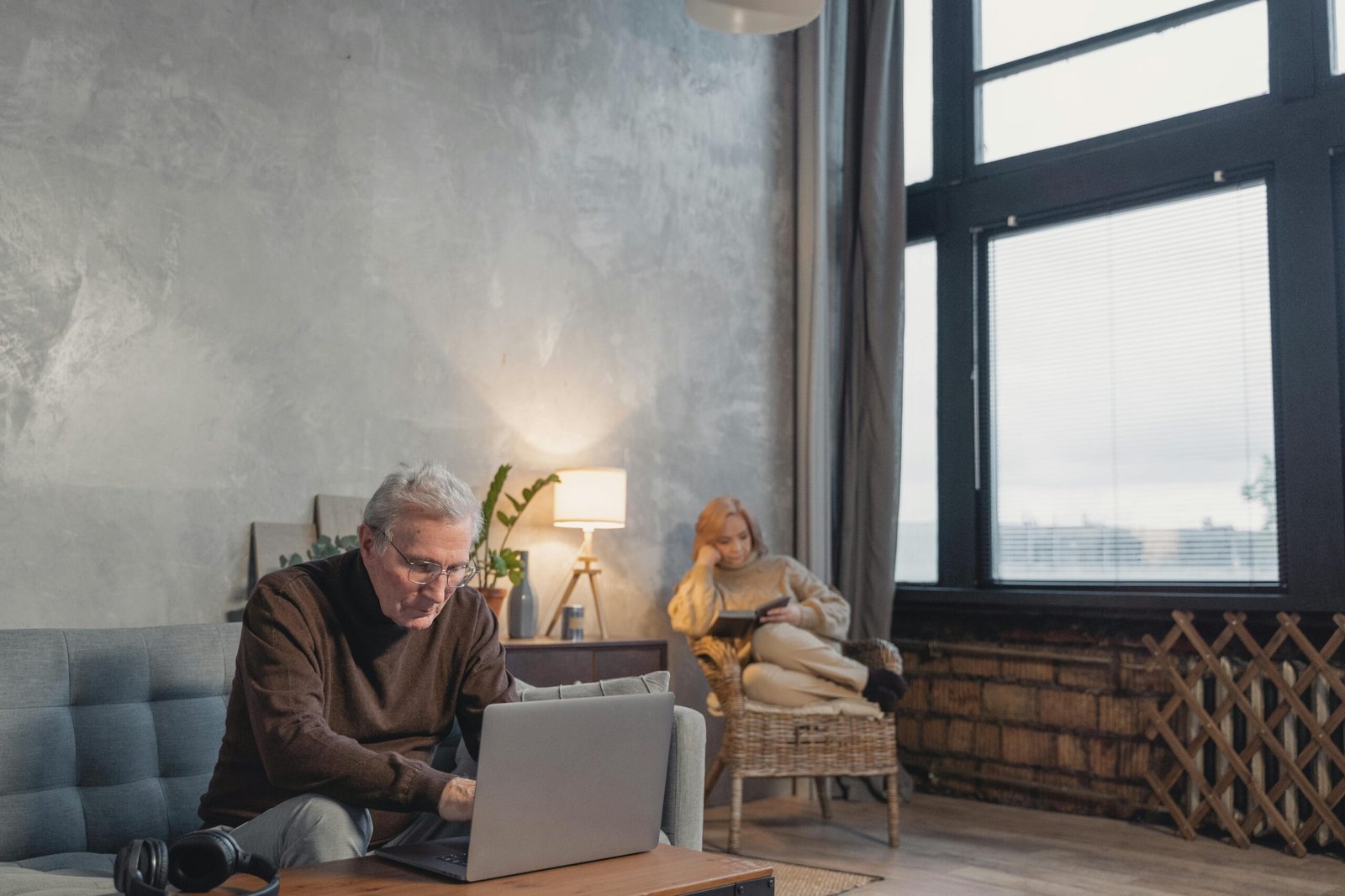 Elderly man working on laptop in modern living room with natural light and decor.